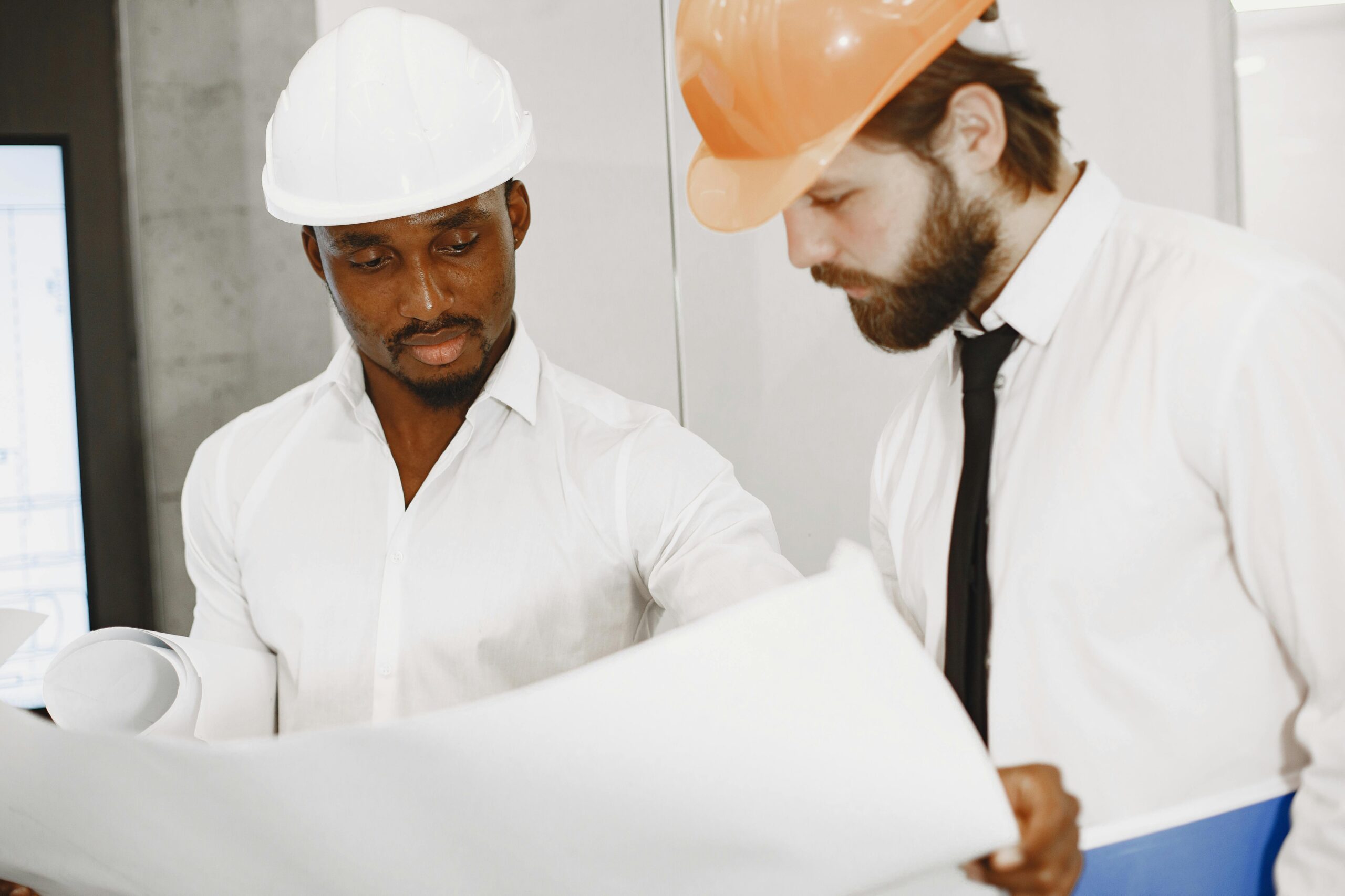 Two contractors in hard hats reviewing blueprints during a home renovation project, discussing construction plans and design details.